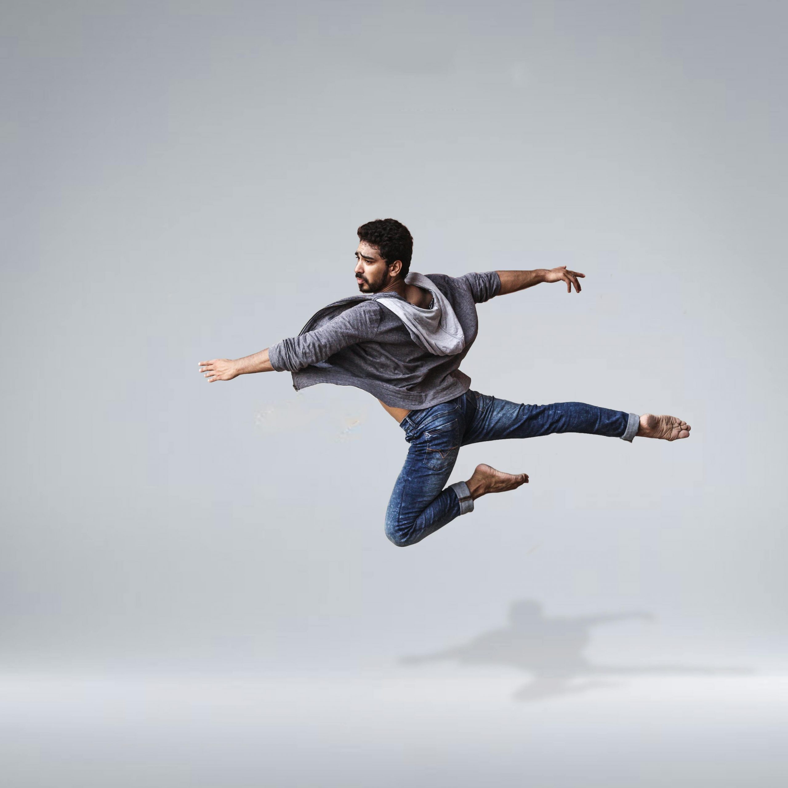 A male contemporary dancer in casual wear leaping gracefully in mid-air, showcasing agility and flexibility.